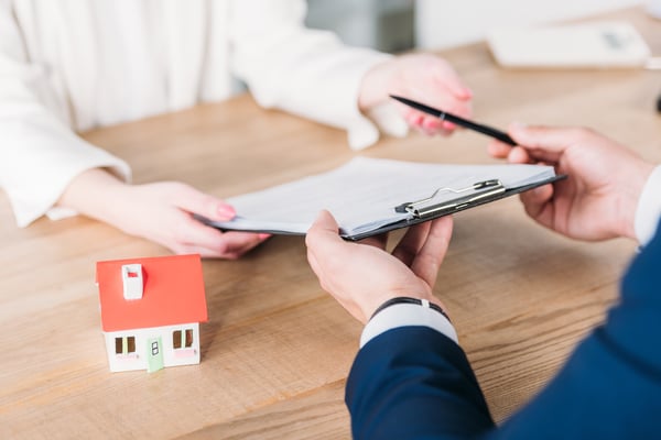 Cropped shot of realtor giving pen and clipboard with loan agreement to customer near house model