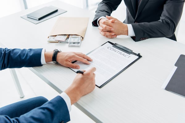 Selective focus of businessman signing document near envelope with bribe and business partner with clenched hands