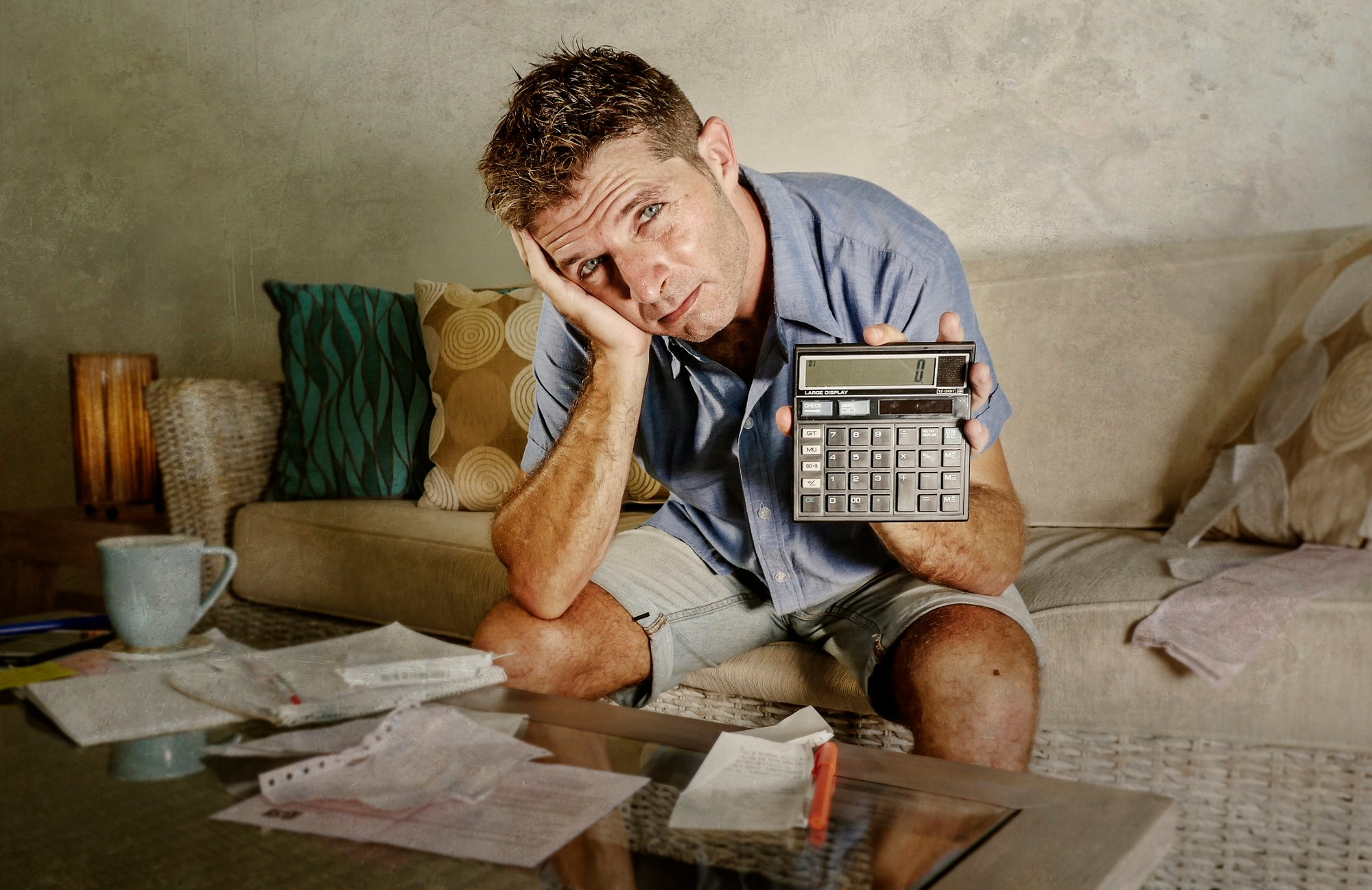 Young attractive worried and stressed man at home calculating month tax expenses with calculator accounting payments doing bank paperwork in stress looking desperate suffering financial problem